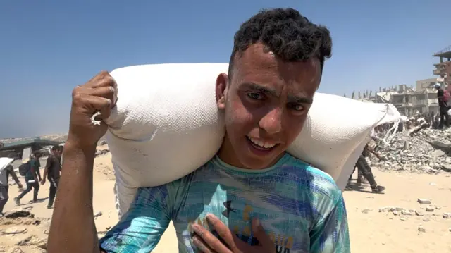 Salah looks at the camera, carrying a white sack of aid on his shoulders