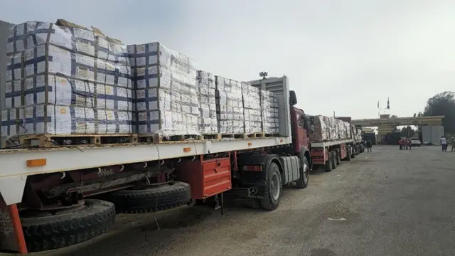 Three lorries with large pallets of aid on the backs queue at a crossing point