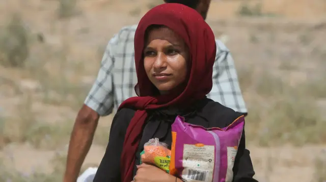 A girl clutching what appears to be a bag of lentils and rice. She's wearing a red head scarf  and looking to her right.