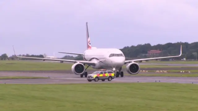 A white plane on a runway with a pickup driving in front of it. The weather is miserable