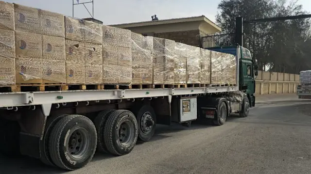 A truck loaded up with pallets enters through a gate, while another truck can be seen having already passed through ahead