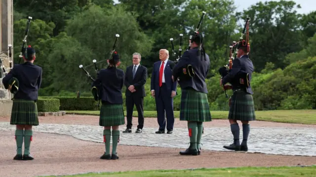 Donald Trump and Keir Starmer look on as bagpipers play for them.