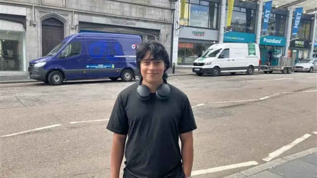Andreas Bermudez stands and smiles at the camera. He has headphones around his neck
