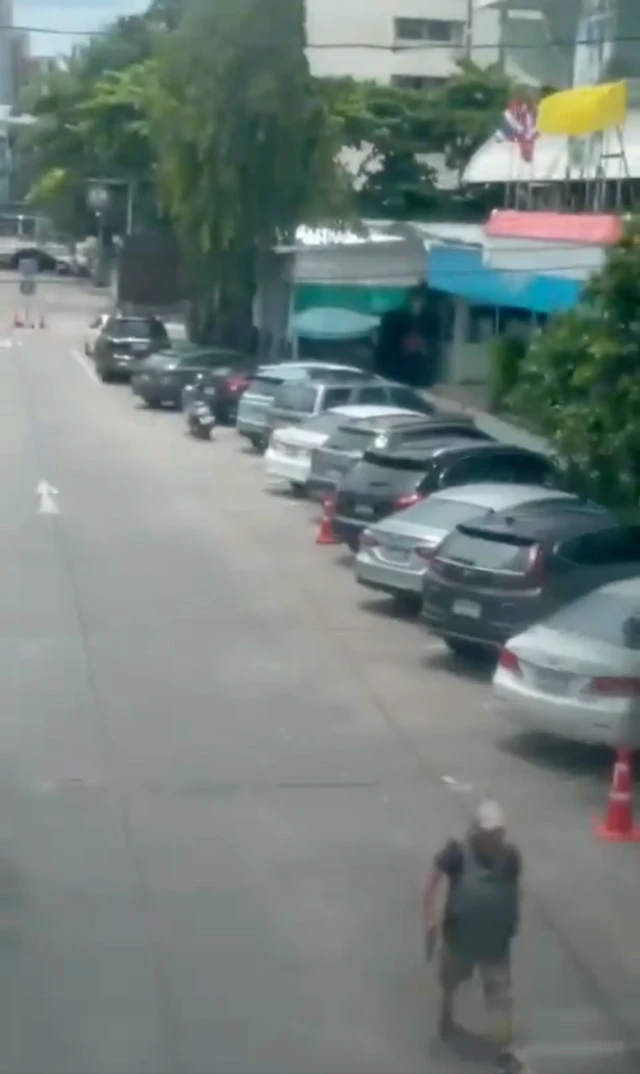 Still from the video of an armed man near the site of a mass shooting in Bangkok. The man is walking on a road and holding what appears to be a gun in his right hand.