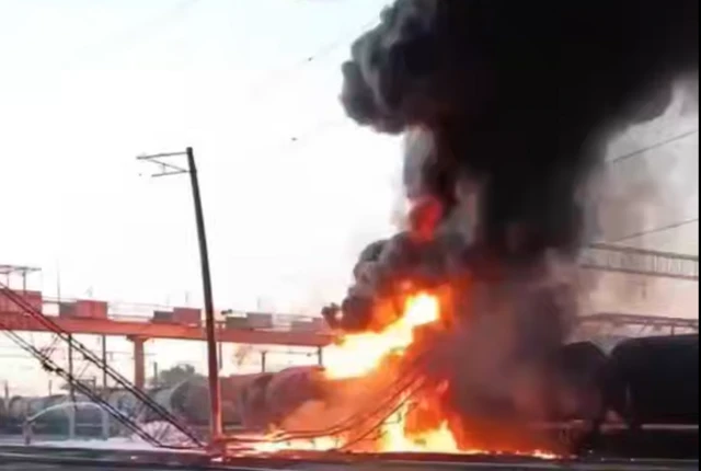 Grab from video showing a huge fire with a plume of dark smoke burning a cargo train tanks