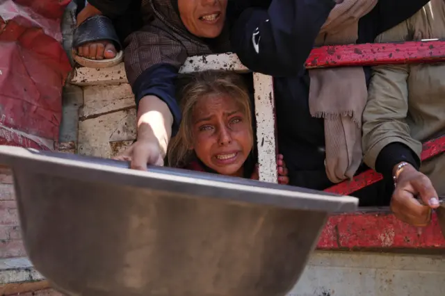 A girl among a crowd of people holding out food bowls.
