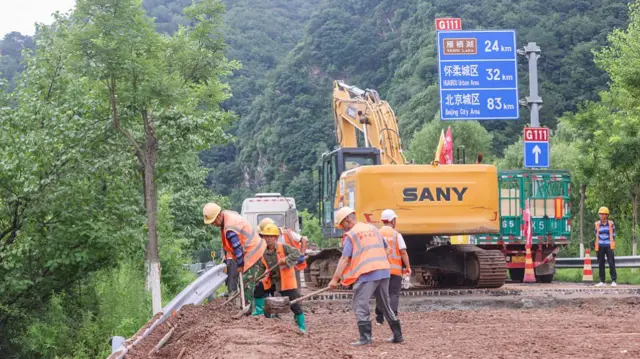Workers in orange vests shovel mud along a road