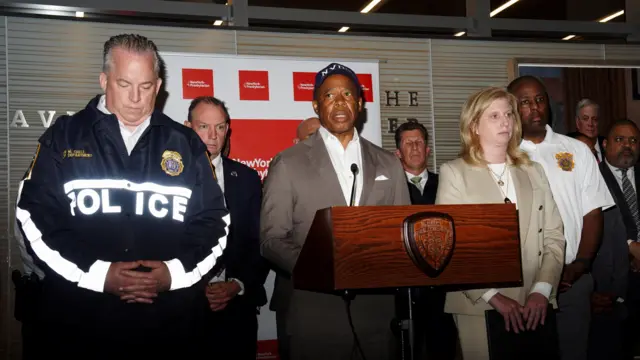 Eric Adams stands at a microphone flanked by people
