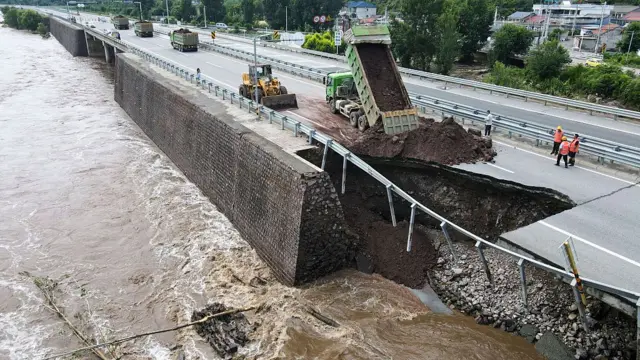 Wide shot of a truck and bulldozer beside a collapsed section of a road