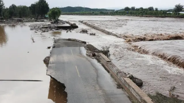 A general view of a damaged road next to the swollen Qingshui river, after a heavy rainfall flooded the area in Miyun district of Beijing
