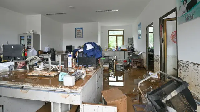 An office flooded with brown water, and furniture and items strewn across the floor