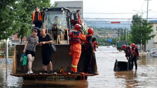 Rescue workers set up a barrier to cover a manhole in the middle of a flooded road, near a front loader carrying rescuers and stranded residents following heavy rainfall in Miyun district