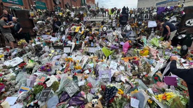 A huge pile of floral tributes and other items at the foot of the Black Sabbath bench in Birmingham.