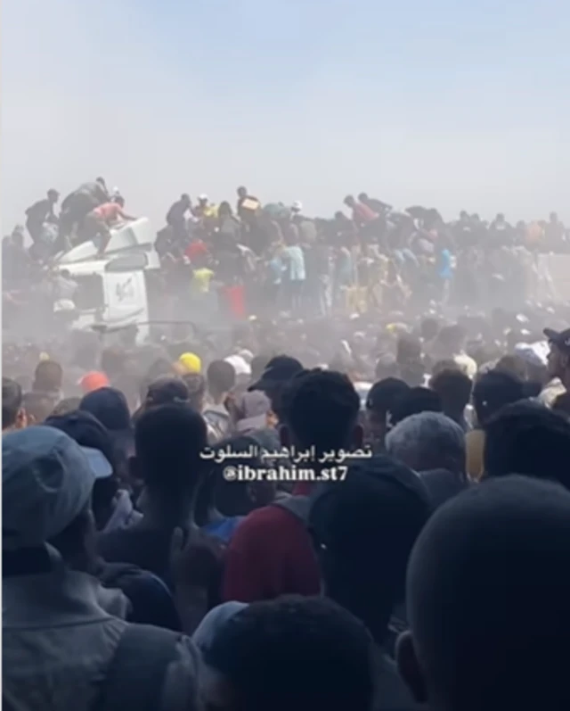 A still image from a video posted to Instagram. It shows a crowd surrounding an aid truck with many people also climbing on top.