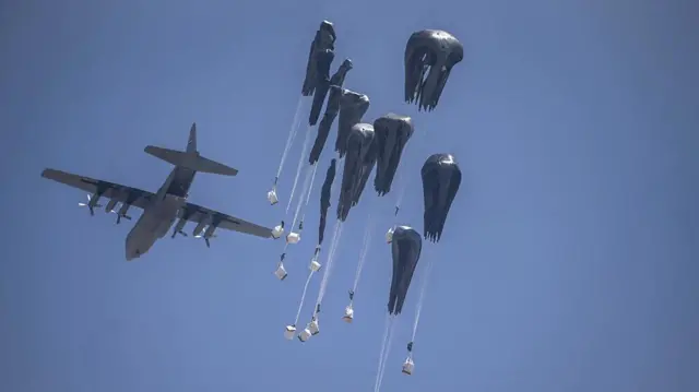 Several white sacks fall from a plane, long parachutes attached to them