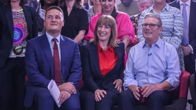 Starmer, Reeves and Streeting sat down smiling, medics stood around them.