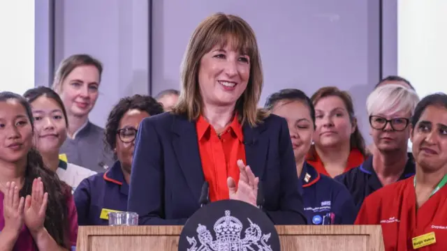 Rachel Reeves, speaking at a lectern, with several medical staff stood behind her.