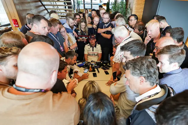 Max Verstappen sits at a table, surrounded by journalists at Silverstone