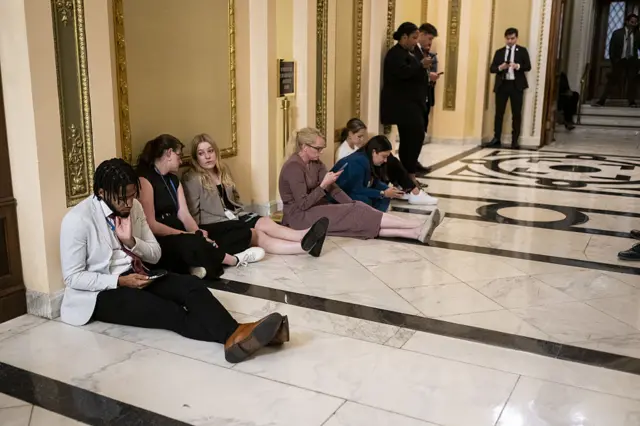 Congressional reporters rest and work sitting on the floor in a Capitol corridor