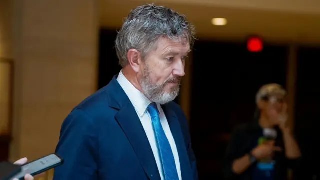 Thomas Massie, wearing a blue suit and tie, looks down as he passes the camera