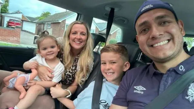 Kirk Ryan and his family seated in a car turn and smile at the camera