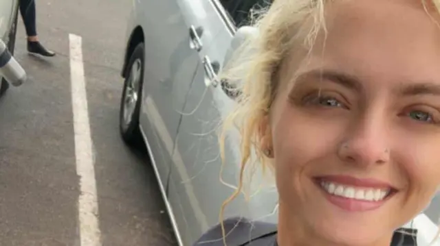 A selfie of Sarah Heavenly Sikes who is wearing a dry or wet suit up against the backdrop of a silver car