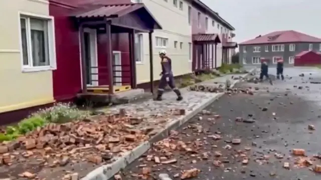 Debris from a damaged building is gathered on the floor as rescuers walk on the residential street.