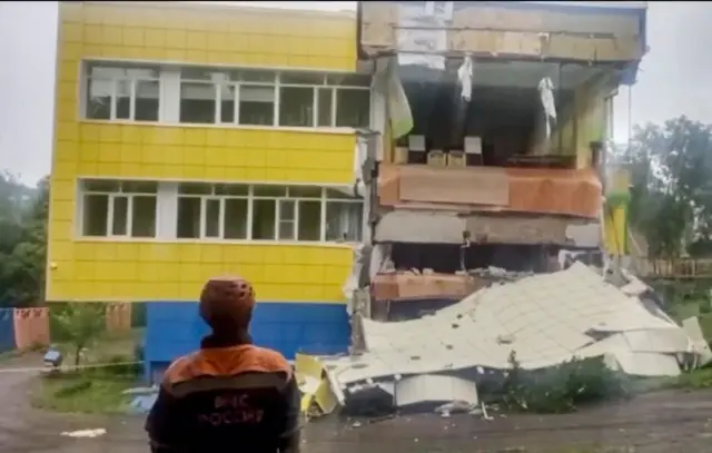 One rescue worker stands looking at the façade of another building which has partially collapsed