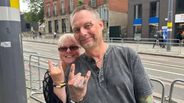 A woman and a man stand on Broad Street. The pair are holding up the Devil's Horn sign/
