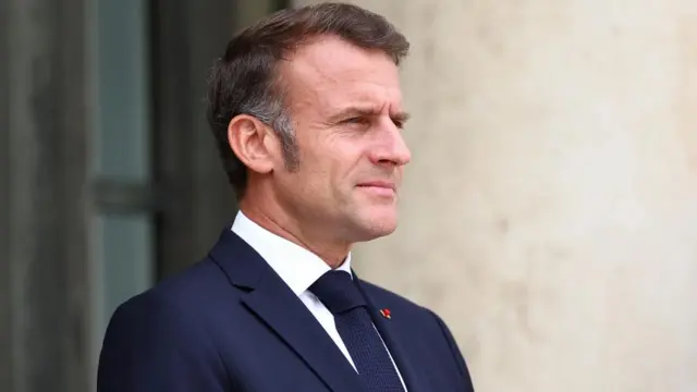 A close up of Macron, who looks to the right with a neutral expression
