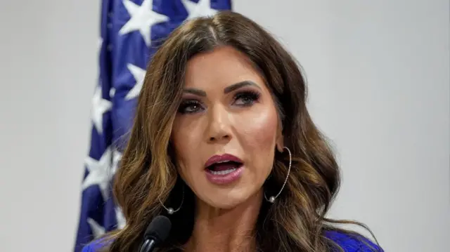 Kristi Noem speaking in front of an American flag