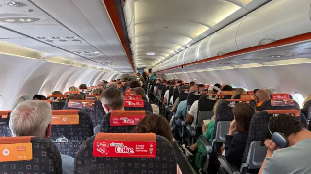 A landscape image of the inside of an easyJet plane with passengers seated in rows