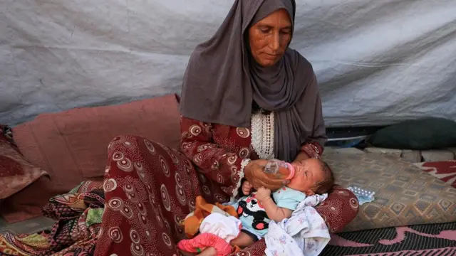 Nemah Hamouda holds her three-month-old granddaughter, Muntaha, in her arms while feeding her with a homemade herbal mixture