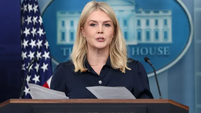 Leavitt in dark blouse holds papers while standing at White House podium