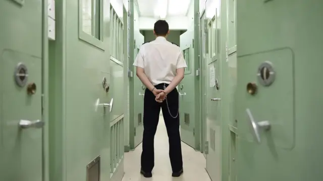 A prison officer stands in between rows of prison cells
