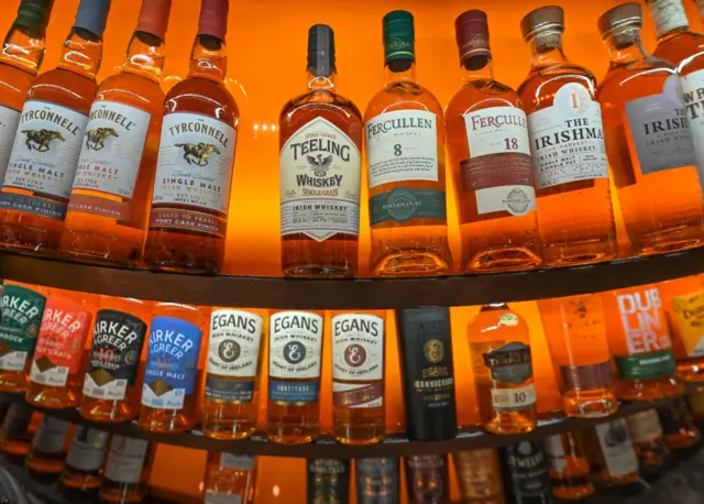 Three curved shelves with bottles of Irish whickey on display, in front of an orange glowing background