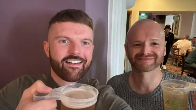 James Caine and Ross Bailey hold drinks up as they take a selfie in a pub