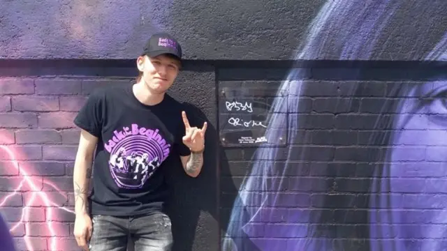 A man standing in front of a street art mural linked to Black Sabbath. Ozzy Osbourne has signed the wall.