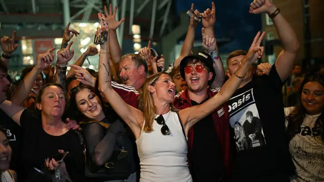 Fans outside stadium with arms in air and singing.
