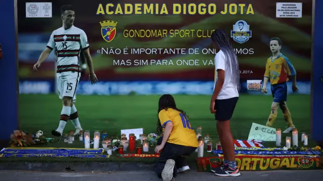 A person kneels in front of a makeshift memorial for Liverpool's Portuguese soccer player Diogo Jota