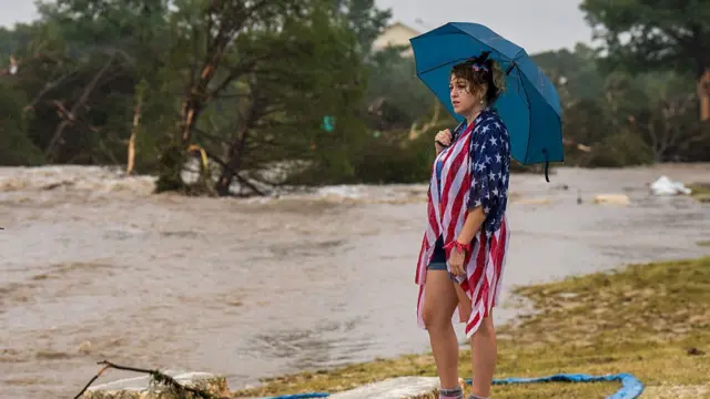 Woman stood on grass looking out at flooded ground, holding umbrella.