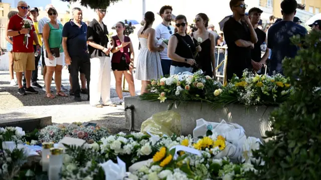 People stand in line near a mass of floral tributes