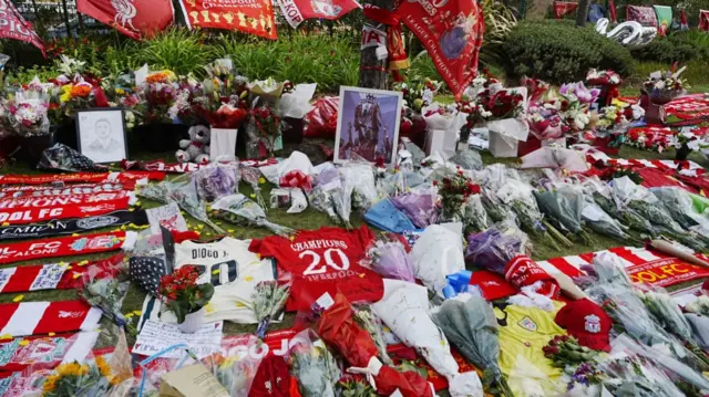 Floral tributes, Liverpool scarves and shirts laid on a grass patch outside Anfield stadium to mark death of Diogo Jota