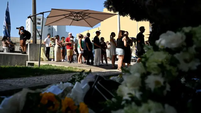 A line of people queue under a sunshade