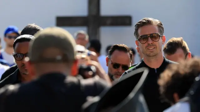 Edwards is photographed wearing a black top and black aviator-style sunglasses
