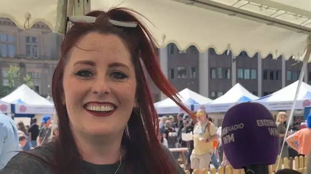 A woman with red hair is sitting in a marquee at a city food festival. She is smiling.