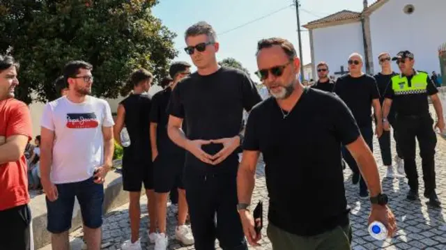 Powe talks along a cobbled street with an official, both wearing black t-shirts