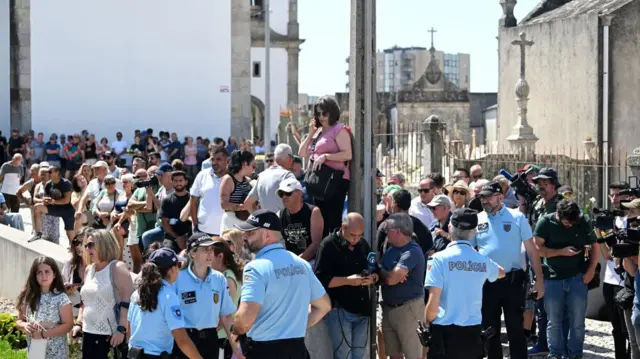 A crowd of several dozen people gathered outside of a church, with police in the foreground