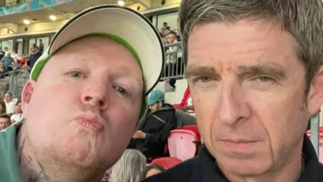 Danny Pearson takes a selfie with Noel Gallager with people sitting on seats at Wembley Stadium behind
