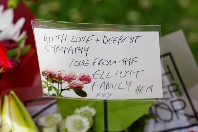 A card attached to a bouquet of flowers reading "With love and deepest sympathy. Love from the Elliot family. HE19"
